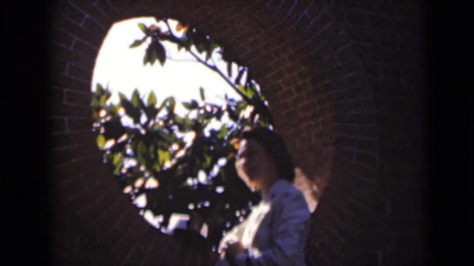At the end of the clip, the woman is still framed by brick masonry and a round opening, with bright foliage behind her profile.