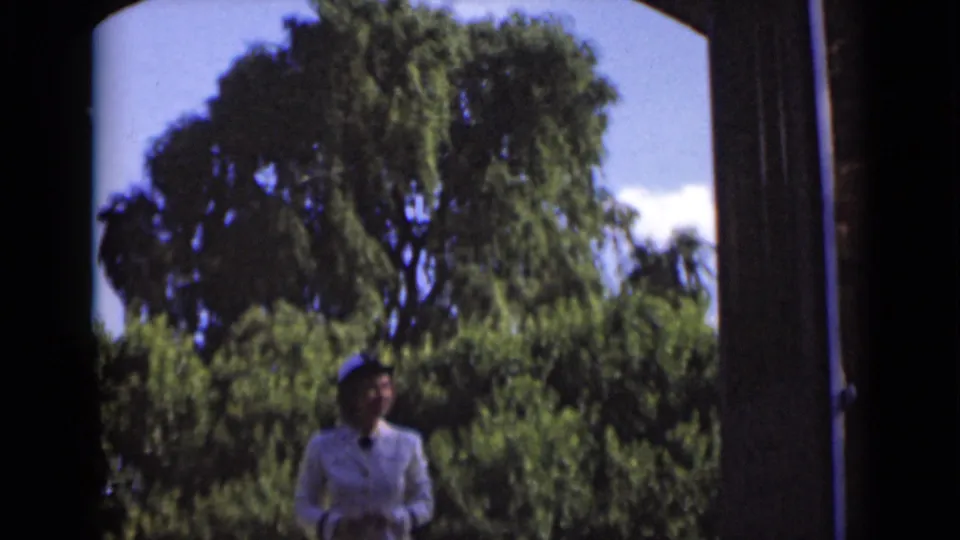 A lower, darker frame shows the woman in a white suit near the doorway opening, with large trees and blue sky dominating the view.