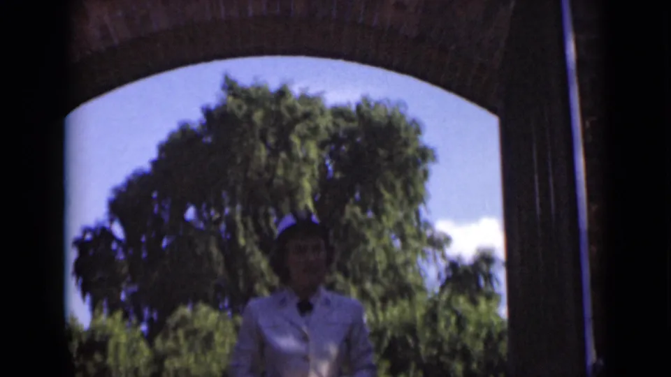 The woman remains partly silhouetted under the arched entrance, with sunlit greenery behind her in the 1947 New York clip.