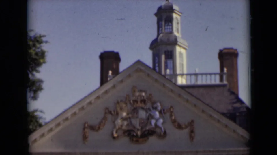 1947 New York home-movie frame showing a historic gabled roof with gilded heraldry, brick chimneys, and a rooftop watch tower against blue sky.
