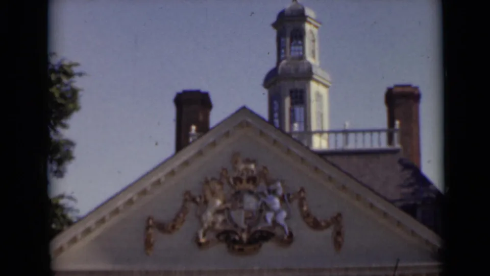 1947 New York frame focusing on the gable, gilded heraldic decoration, chimneys, and rooftop tower, with handheld home-movie softness.