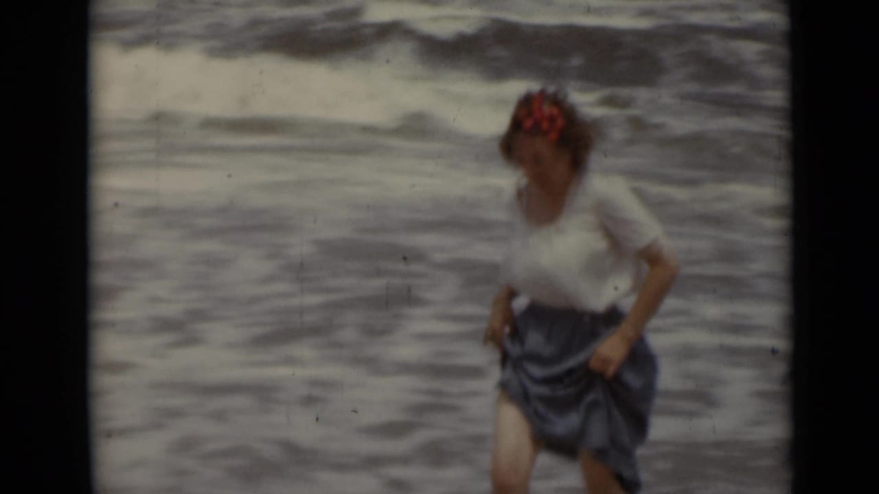 Woman in a white blouse and blue skirt runs near ocean waves.