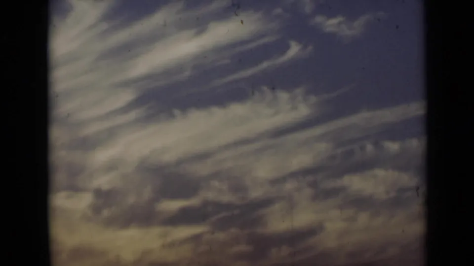A soft, grainy home-movie view of streaked clouds and sky, likely following the beach scene.
