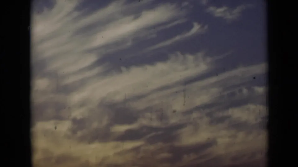 The 8mm frame shows a textured cloudy sky with faded color and visible archival film grain.