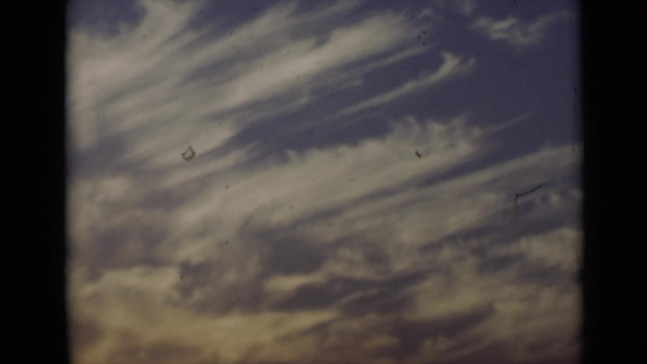 1947 New York 8mm frame showing streaked clouds in a blue-purple sky with warm lower tones and film-edge shadowing.