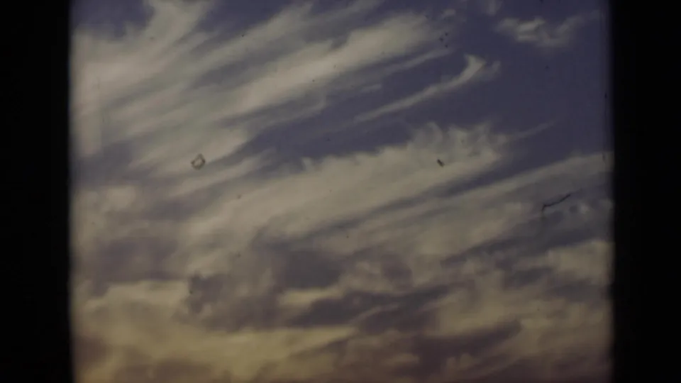 1947 New York 8mm frame showing streaked clouds in a blue-purple sky with warm lower tones and film-edge shadowing.
