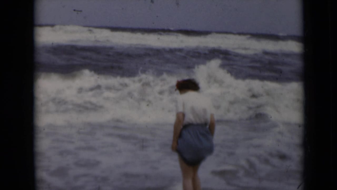 Woman in blue shorts stands at the edge of breaking ocean waves.