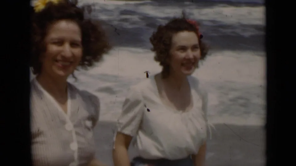Two women smile near the New York shoreline, their hair and clothing moving in the wind in 1947 home-movie footage.