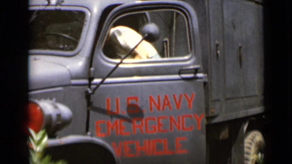 In 1947 New York footage, a woman is visible through the open driver's window of a gray U.S. Navy emergency vehicle.