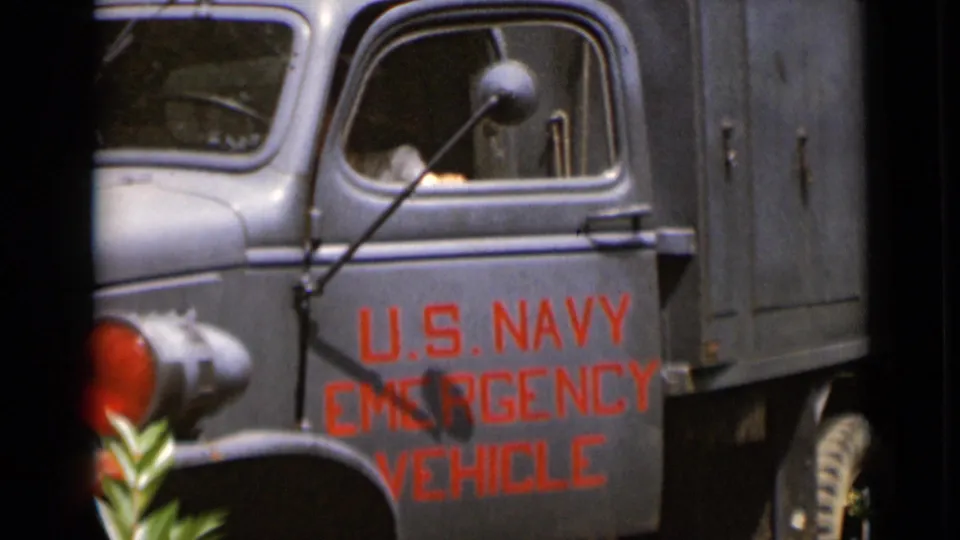 The gray U.S. Navy emergency vehicle is framed close up, with red door lettering and a person partly visible in the cab.