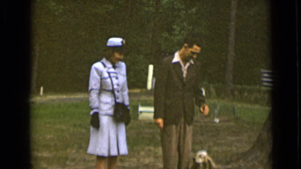 1947 New York home-movie frame showing the couple in formal clothing continuing through a grassy park with the dog near the lower edge.