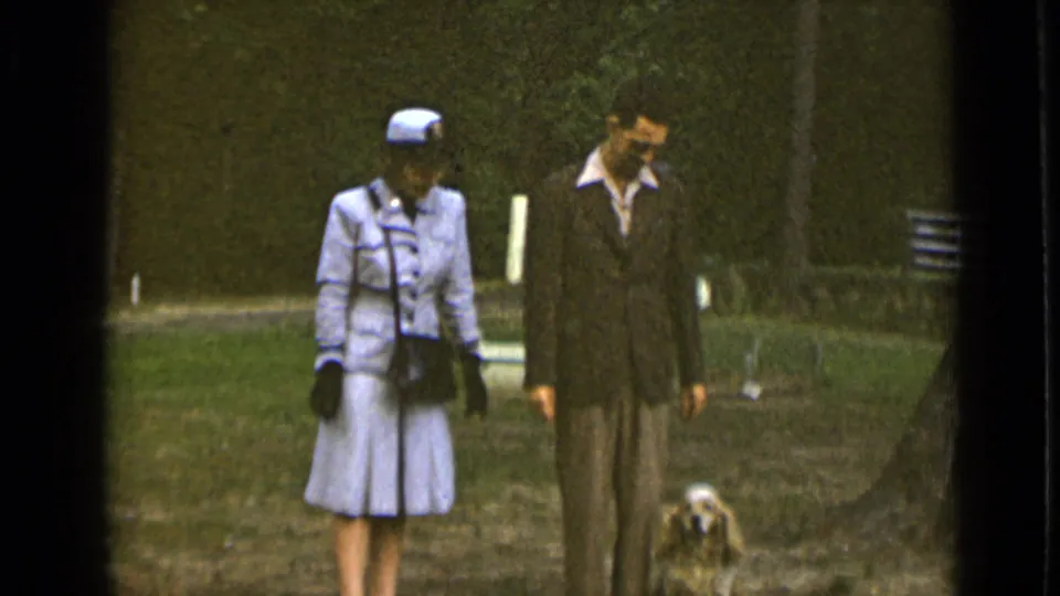 1947 New York park frame with the couple and small dog visible near a tree and bench in soft 8mm color.