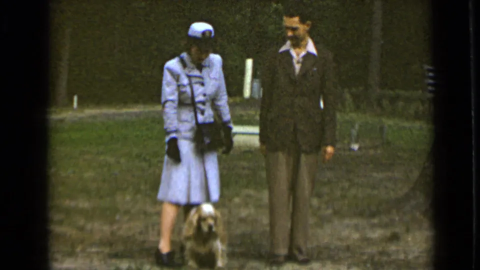 The 1947 New York park scene shows the woman in a pale uniform and hat standing with a suited man and small dog.