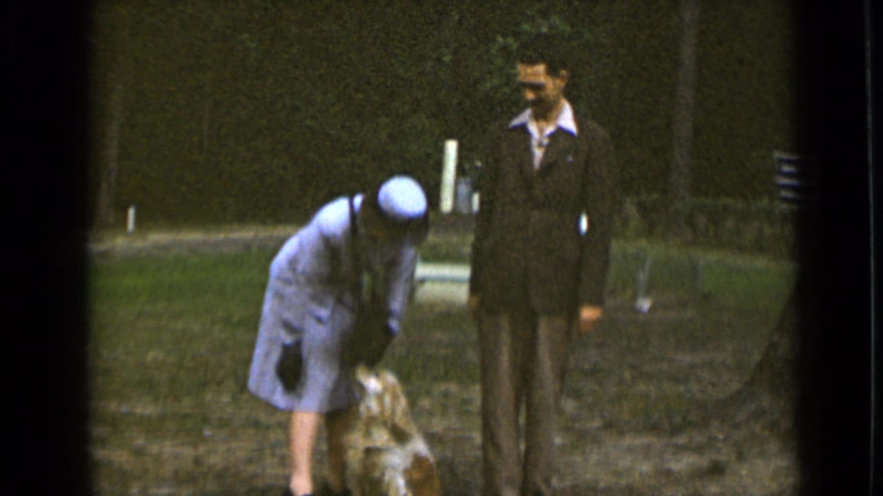 The woman continues bending toward the small dog as the suited man looks on in the 1947 New York park scene.