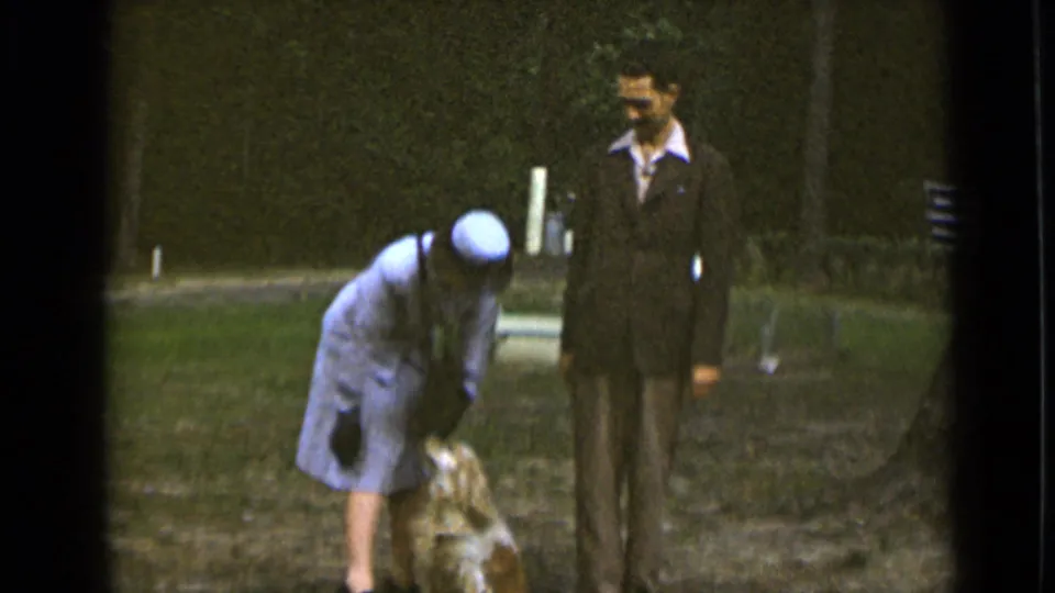 The woman continues bending toward the small dog as the suited man looks on in the 1947 New York park scene.