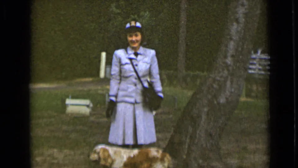 A smiling woman in 1947 New York footage faces the camera while a small dog stands partly visible at the bottom of the frame.