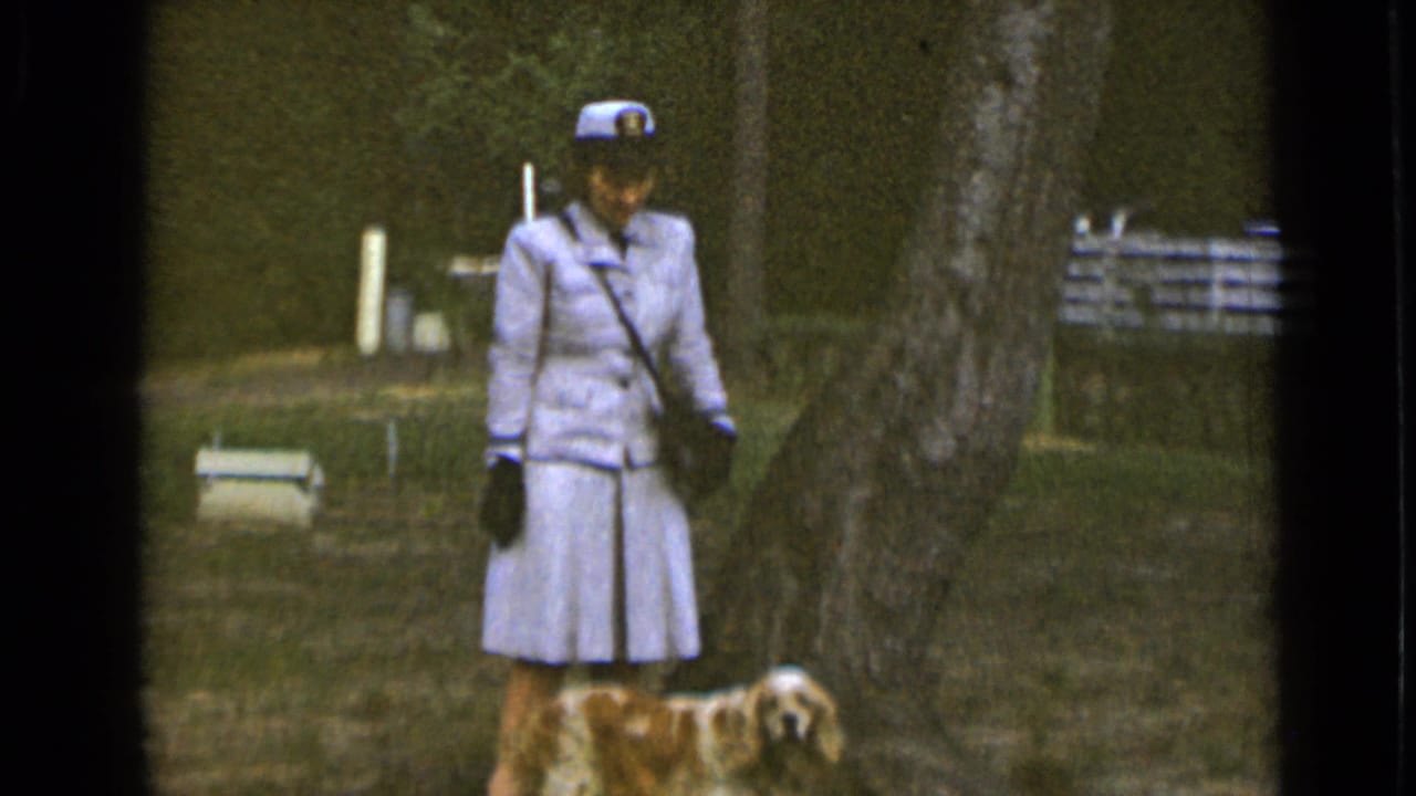 Uniformed woman faces the camera as her spaniel walks beside her in the park.