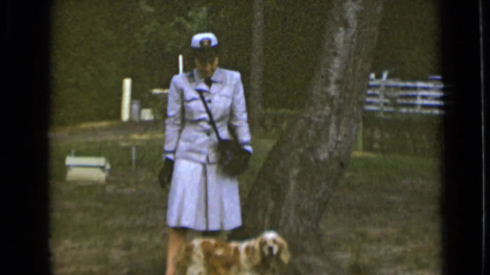 The 1947 park scene shows a woman in a tailored light uniform standing near a tree as her golden spaniel looks toward the camera.