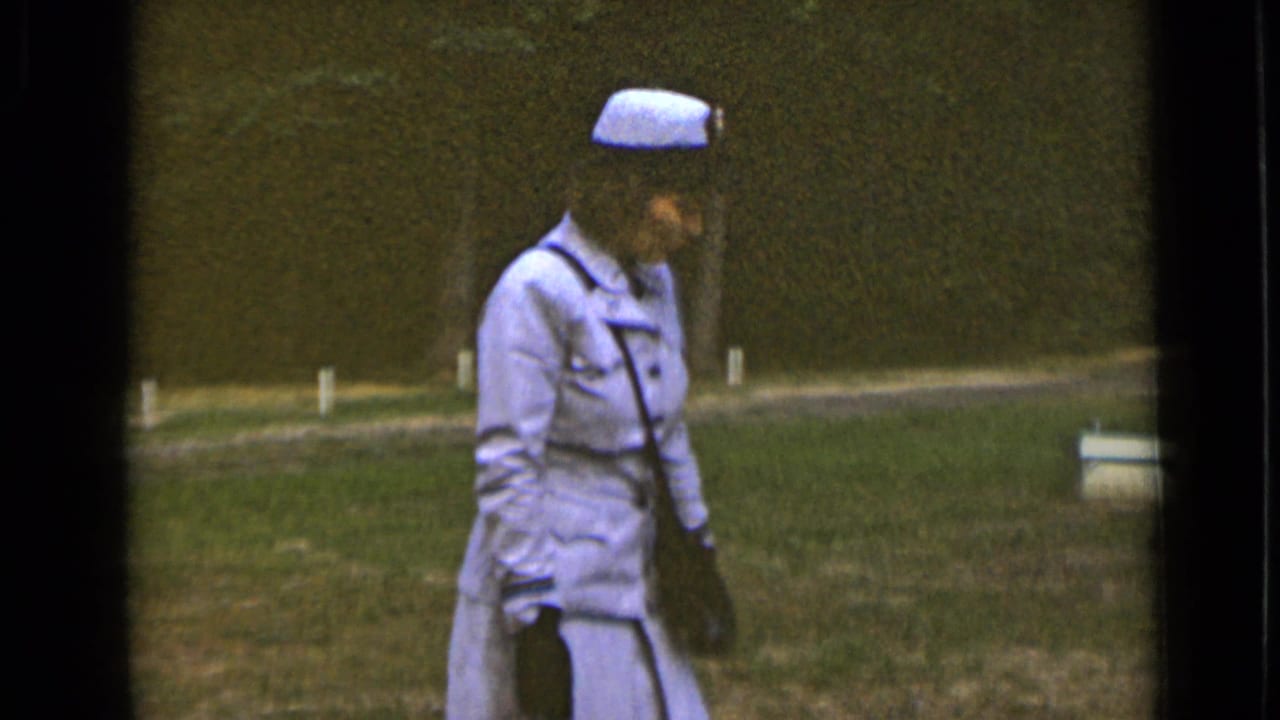 Woman in a light uniform and cap walking across a grassy field.