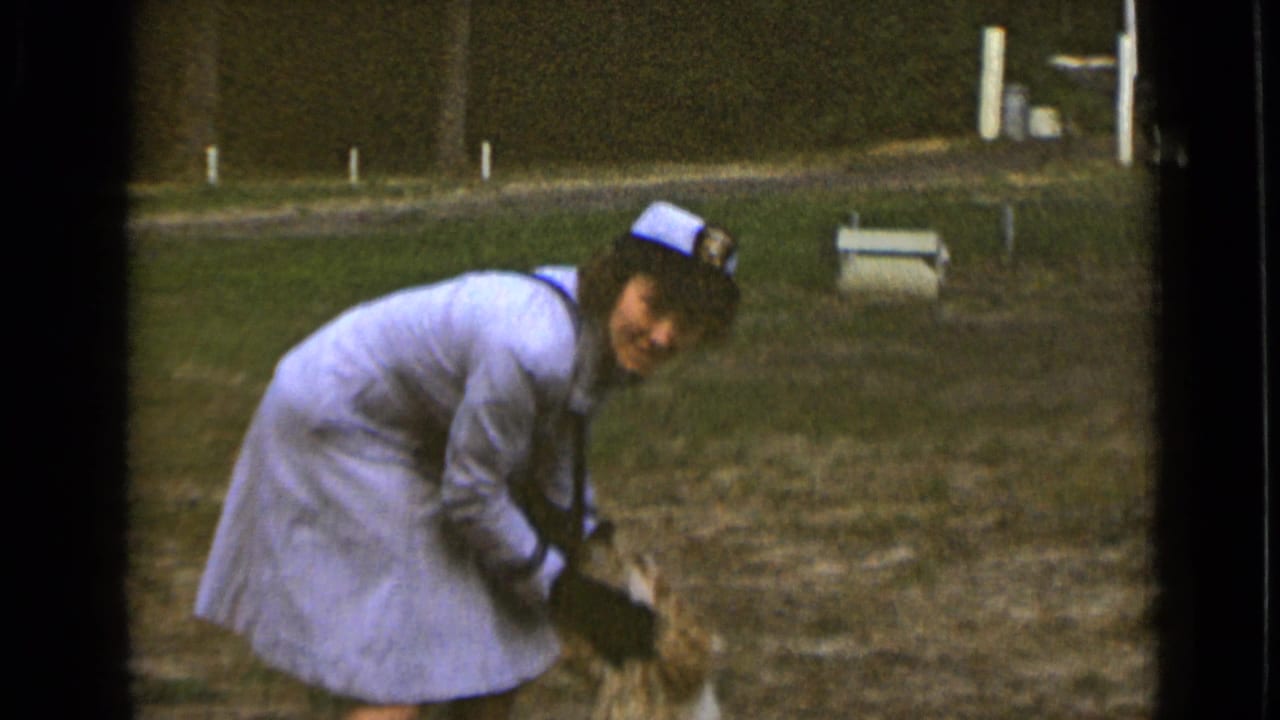 Woman bending down in a field while smiling toward a dog near her hands.