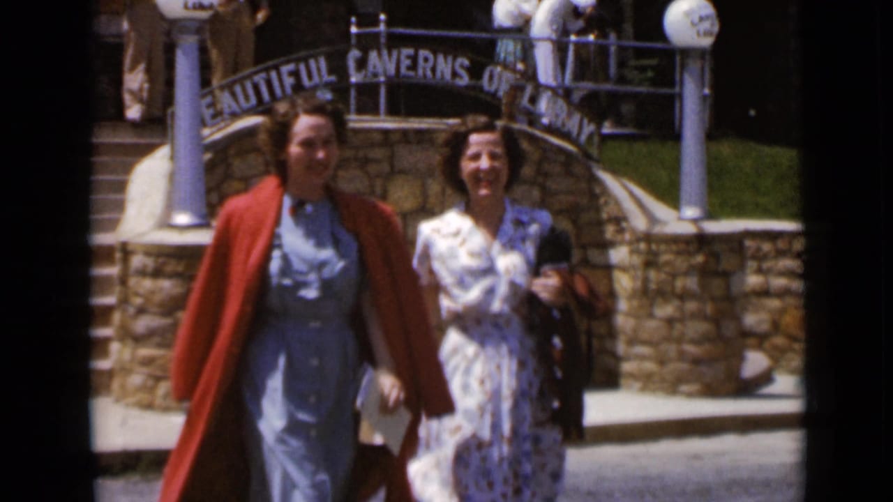 Two women walk near a stone arch with Caverns of Luray signage.