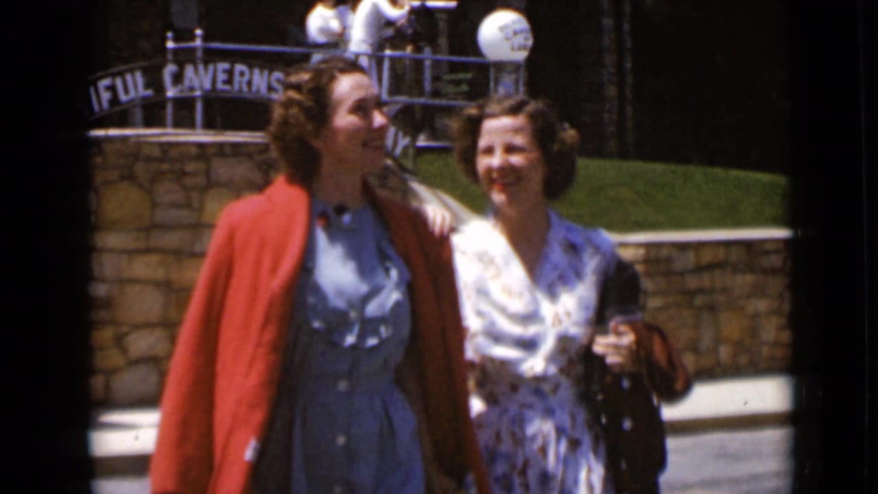 Two smiling women walk arm-in-arm past the stone tourist entrance.