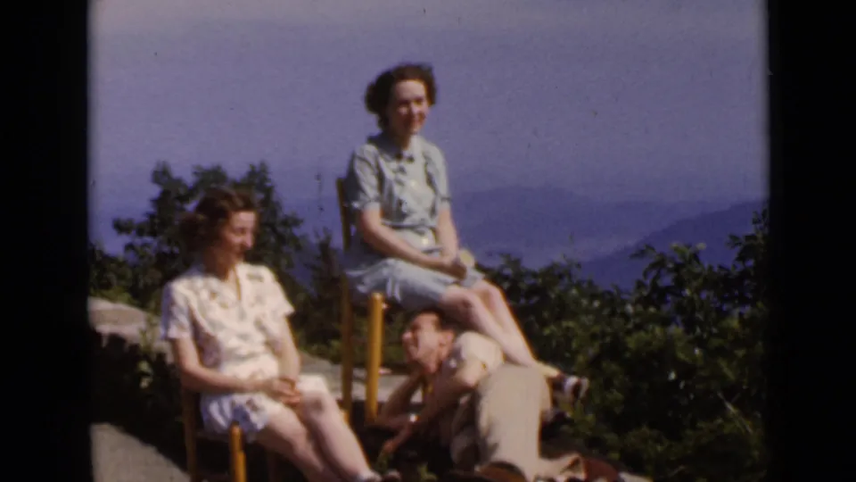 1947 New York home-movie still of two women in light dresses sitting outdoors as a man reclines beside them.