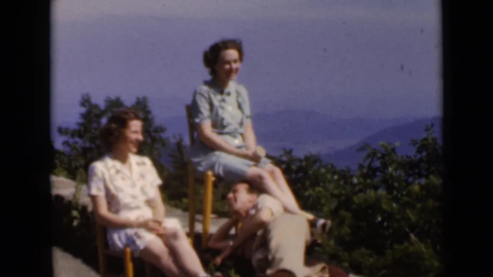 1947 New York outdoor family footage frame with two seated women and a reclining man in a sunny hillside setting.