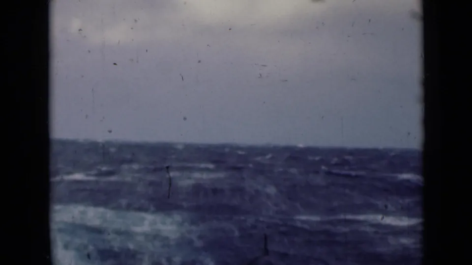 1940s 8mm shipboard view of rough blue water and a low horizon, with visible dust and dark frame borders.