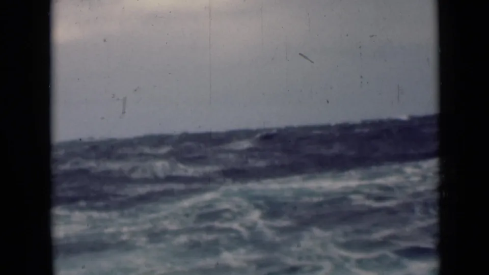 A rough open-sea view on 8mm film shows a slightly tilted horizon, white foam, blue water, and visible dust marks.