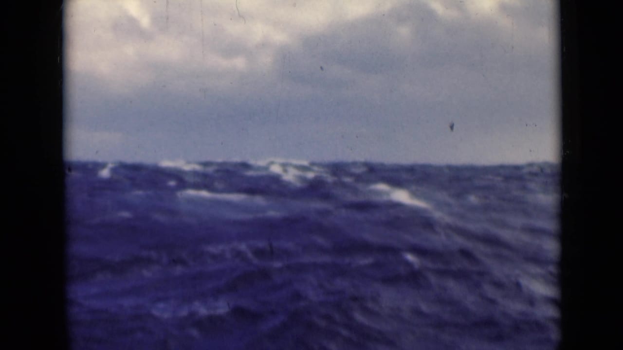 1947 Persian Gulf home-movie frame showing large ocean swells beneath a cloudy sky, viewed through dark vertical framing.