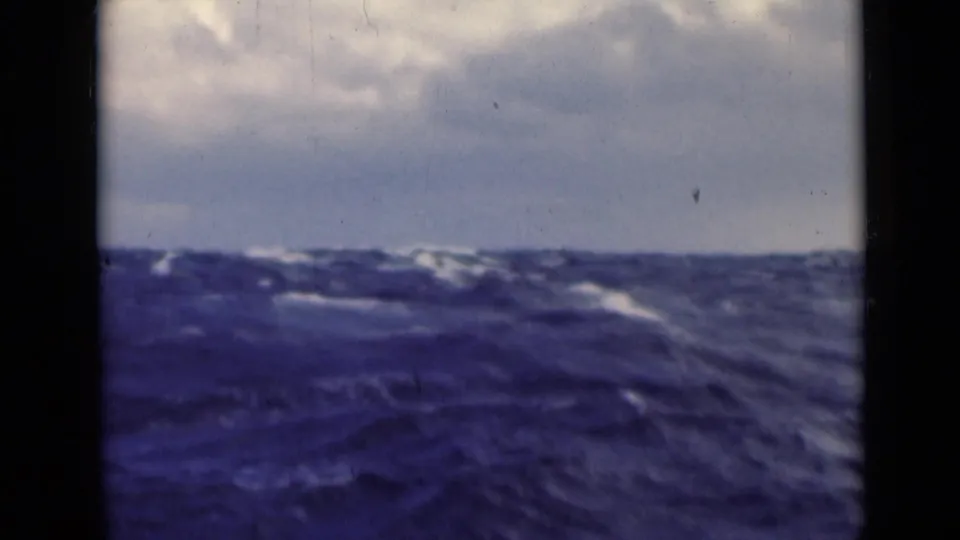1947 Persian Gulf home-movie frame showing large ocean swells beneath a cloudy sky, viewed through dark vertical framing.
