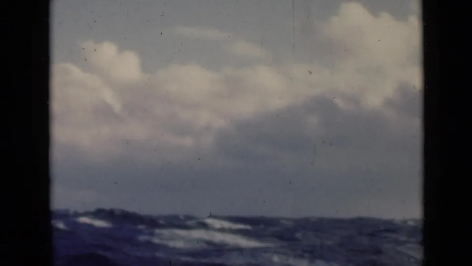 Archival 8mm view of choppy water and cloud cover, with a dark vertical frame dividing the boat-side view.