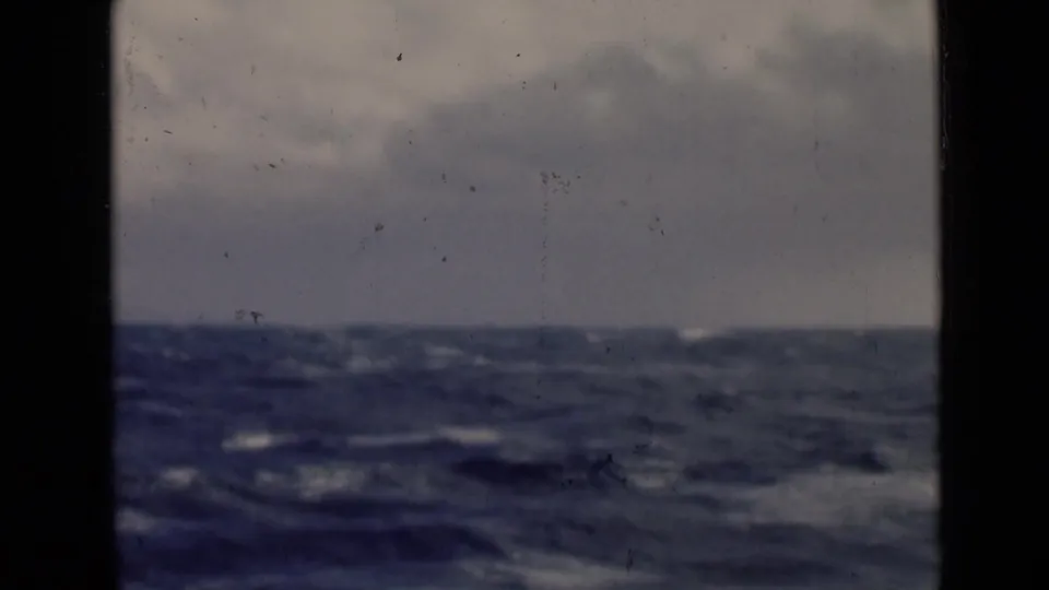Soft 8mm frame of rough open water beneath an overcast sky, with dark gate edges and visible film wear.