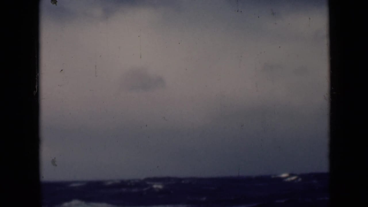 Dark blue ocean waves under a muted cloudy sky with film-frame borders.