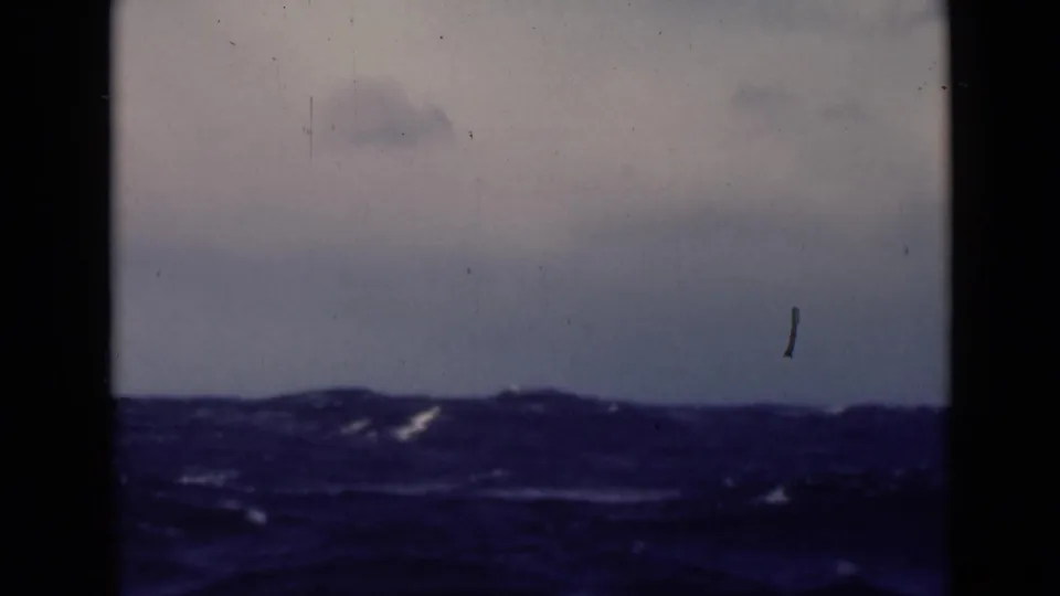A rough sea fills the lower frame, with small whitecaps and a dim horizon in archival 8mm footage.