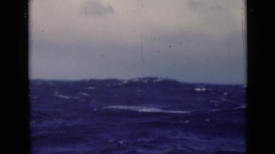 The frame shows dark rolling waves and a cloudy horizon, with visible dust and edge shadows from the 8mm scan.