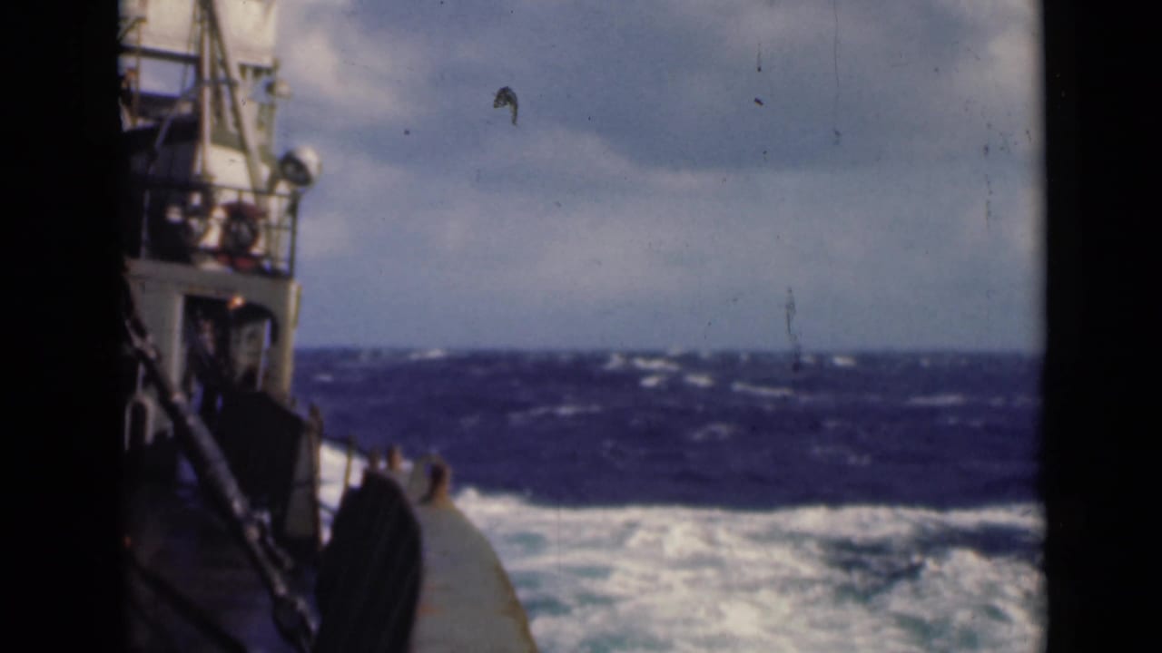 Ship structure at left with dark rolling waves and bright cloud cover across the horizon.