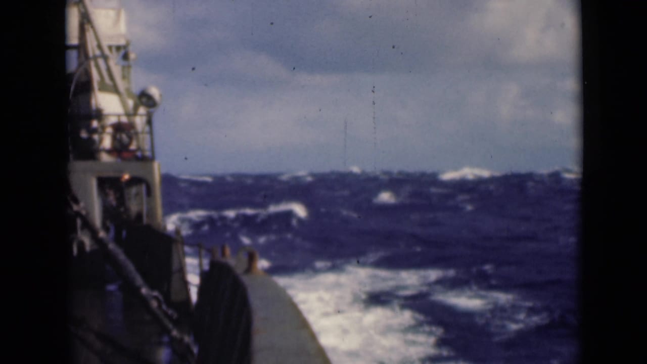 Vessel side and deck fittings above white wake and dark waves.