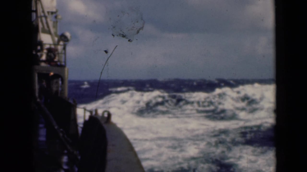 Rough sea seen past part of a ship with white waves across the horizon.