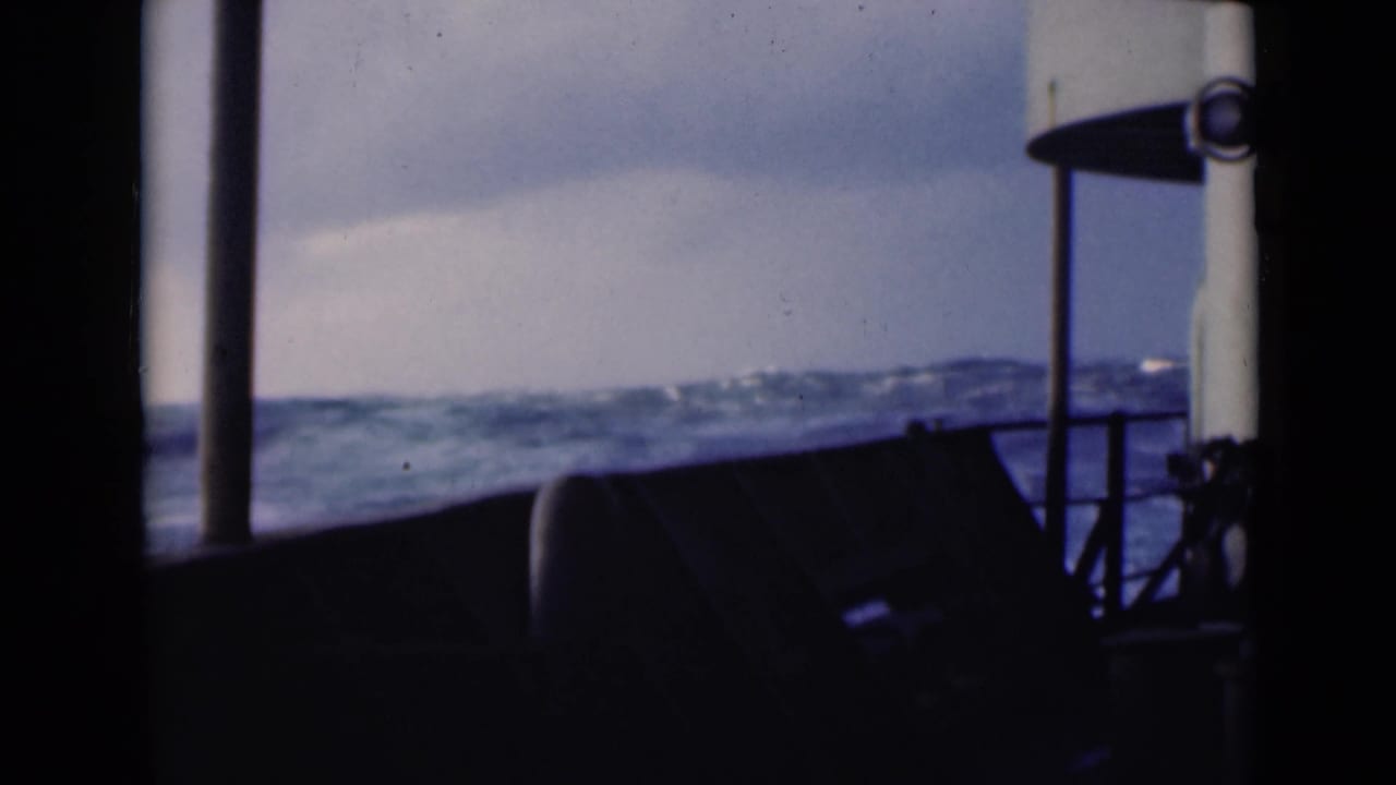 Choppy sea seen through dark boat-window posts and railing.