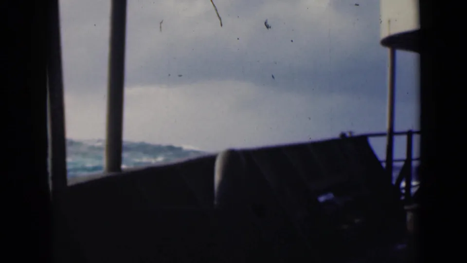 1947 8mm shipboard view over choppy Persian Gulf water, with deck railings and vertical supports in silhouette.
