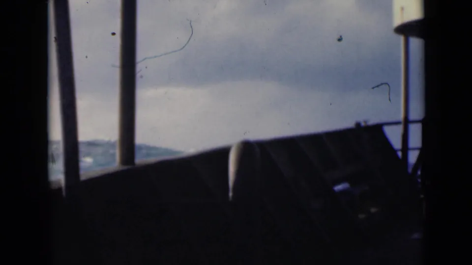 Shipboard 8mm frame looking past dark railings toward rough Persian Gulf water beneath a cloudy horizon.