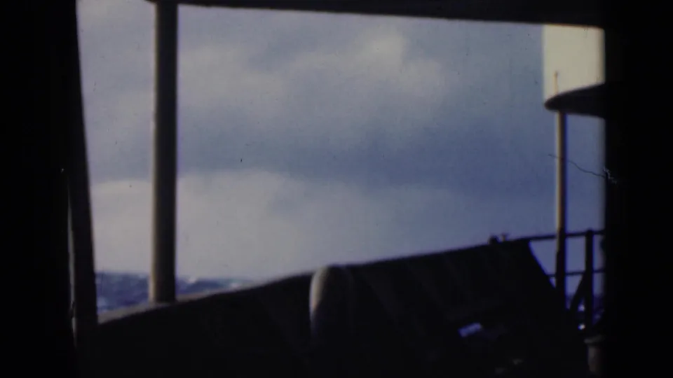 Home-movie frame from a ship looking out over blue-gray Persian Gulf water through dark deck railings.