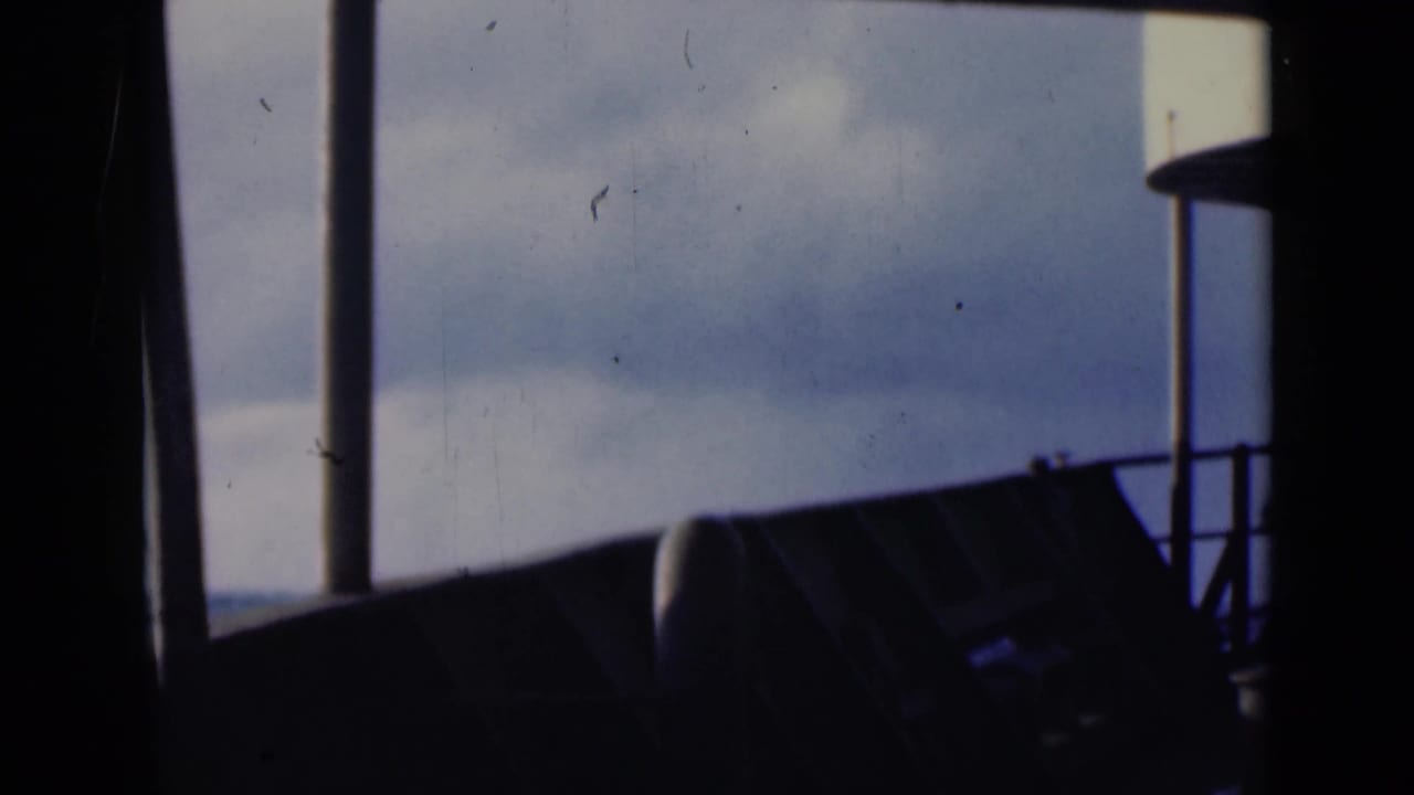 1947 8mm frame from a vessel, with silhouetted window bars, railings, and cloudy sky visible through the opening.