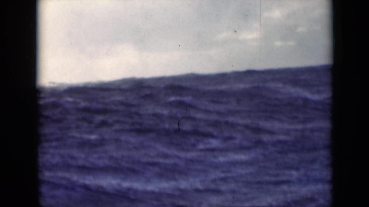 Dark ocean swells beneath a cloudy sky with vertical ship-side framing.