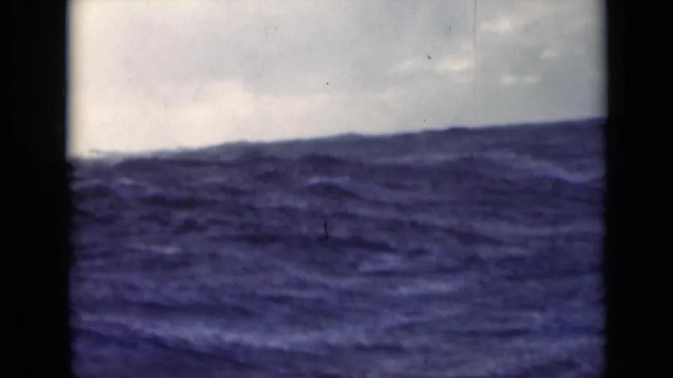 1947 8mm frame of rough open water under clouds, seen from a ship with dark vertical framing at the edges.