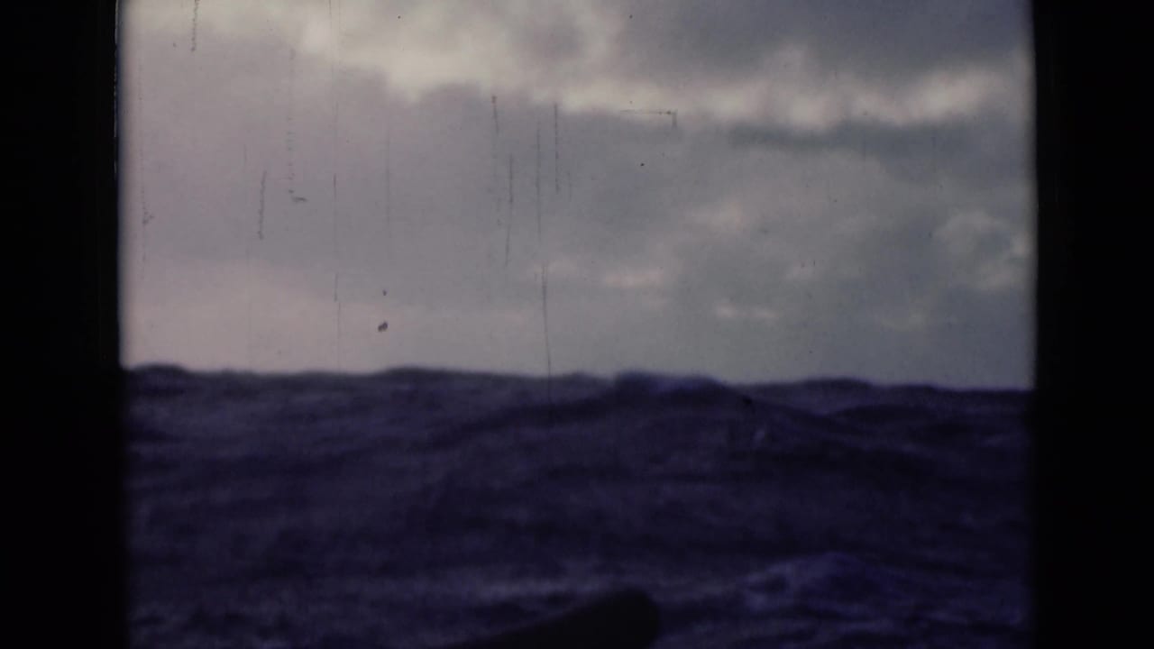 1940s 8mm home-movie frame of rough open water beneath clouds, with dark gate edges and vertical frame division visible.