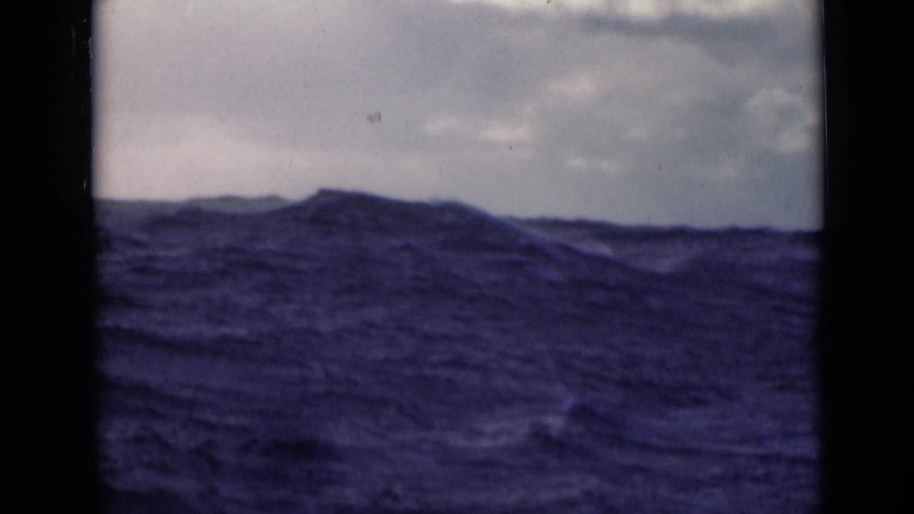 Large blue wave rising below a cloudy sky, framed by dark film borders.
