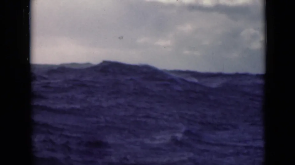 Rough open sea with a broad swell and cloudy sky, captured on color 8mm footage from a likely moving vessel.